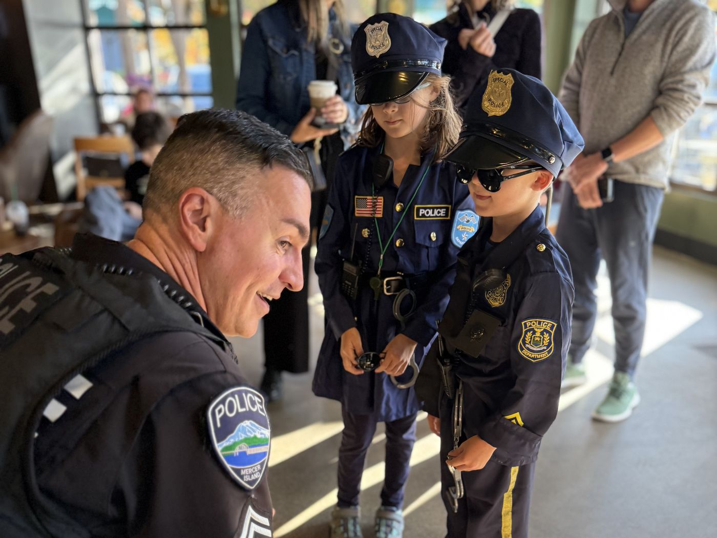 A Mercer Island police officer kneels to greet two children dressed in police uniforms at Coffee with a Cop.