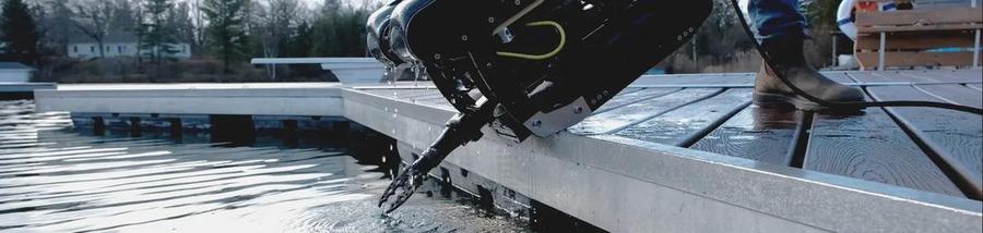 A compact underwater drone with a grabber arm being lowered into a lake from a dock
